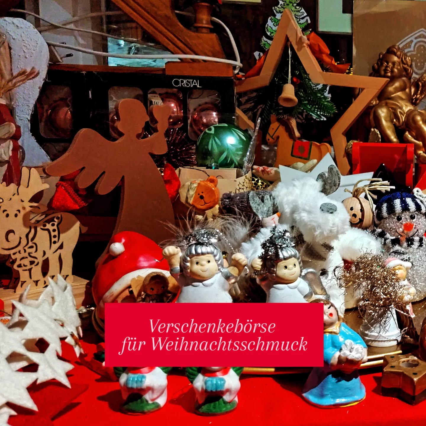 Dieser Alternativtext wurde KI-generiert: Eine farbenfrohe Sammlung von Weihnachtsdekorationen, darunter Figuren und Anhänger, steht auf einem roten Tisch. Im Vordergrund befindet sich ein Schild mit der Aufschrift 'Verschenkbörse für Weihnachtsschmuck'.