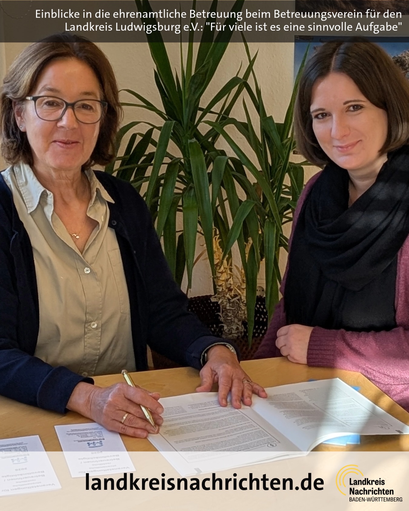 Dieser Alternativtext wurde KI-generiert: Zwei Personen sitzen an einem Tisch und arbeiten mit Dokumenten. Im Hintergrund sind Pflanzen zu sehen, das Bild ist farbig.