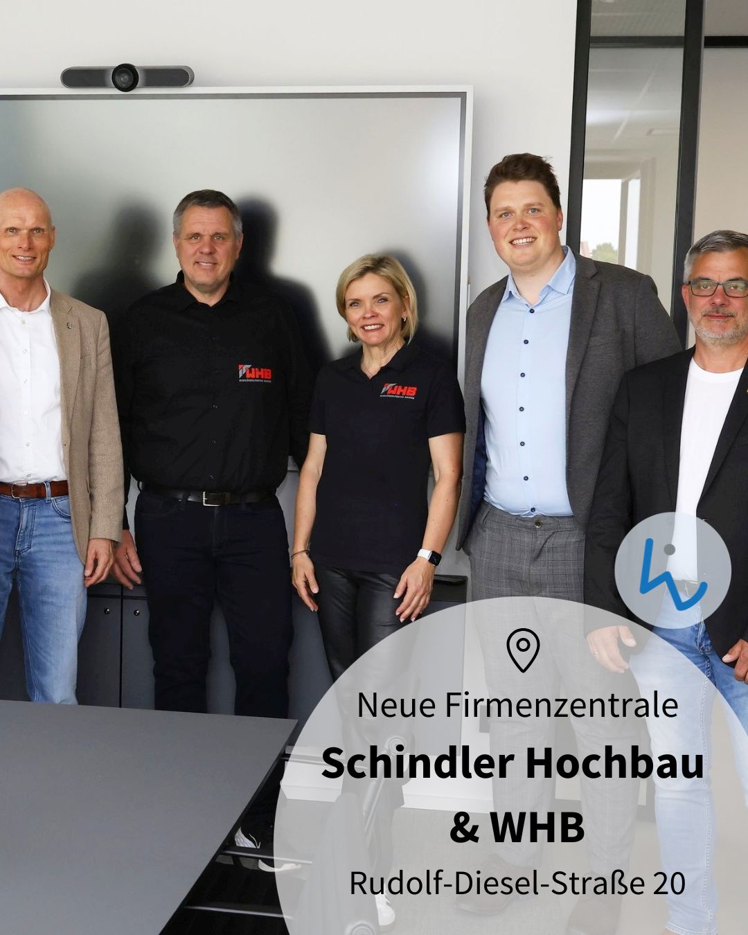 Dieser Alternativtext wurde KI-generiert: Eine Gruppe von Personen steht vor einer gläsernen Fassade. Im Vordergrund befindet sich ein Informationsschild mit Text und einem Standortsymbol.