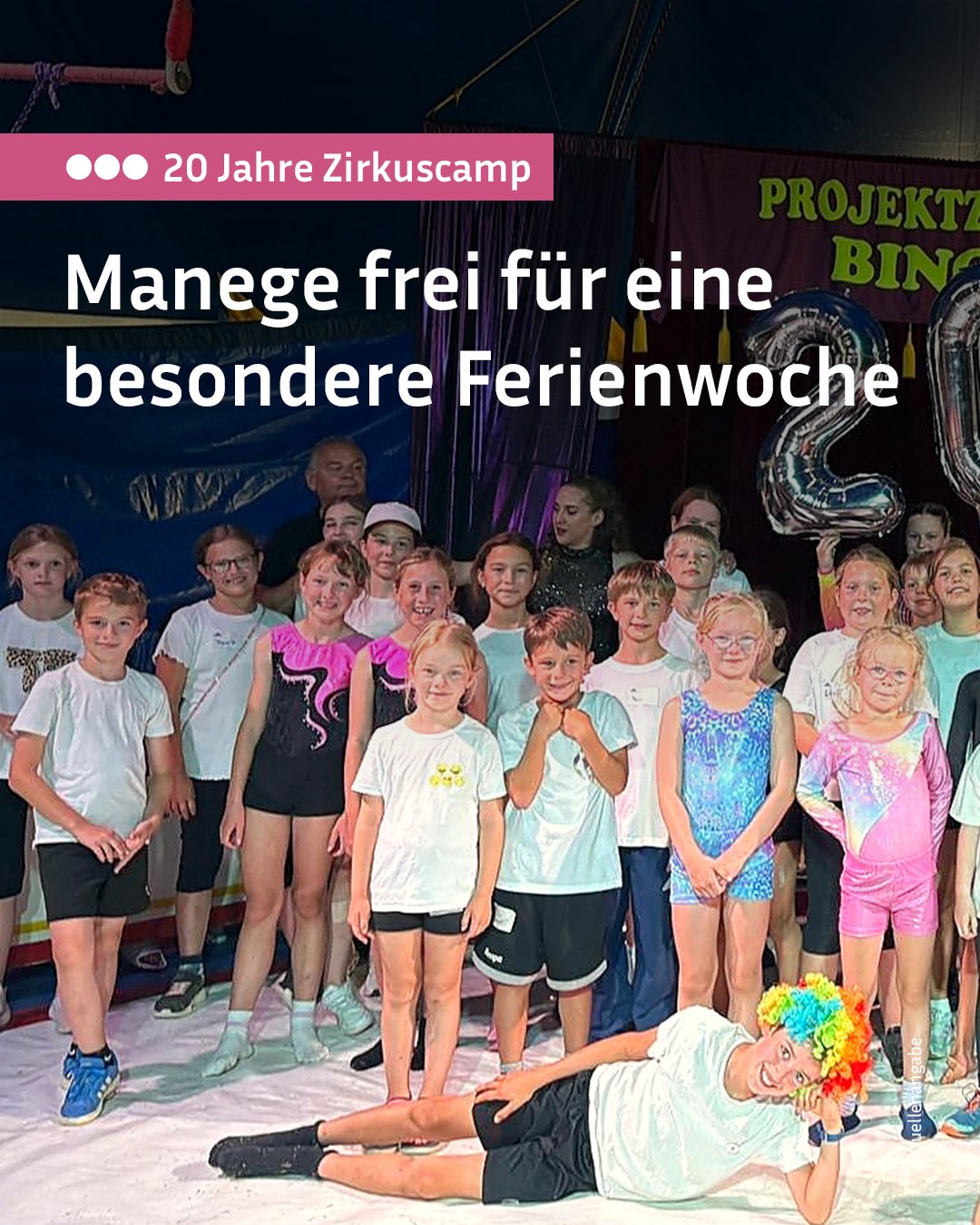 Über dem Bild steht in einem rosa Kasten "20 Jahre Zirkuscamp" und groß "Manege frei für eine besondere Ferienwoche". Eine Gruppe von Kindern und Erwachsenen steht auf einer Bühne, während im Vordergrund eine Person mit bunter Perücke auf dem Boden liegt. (KI-Alternativtext)