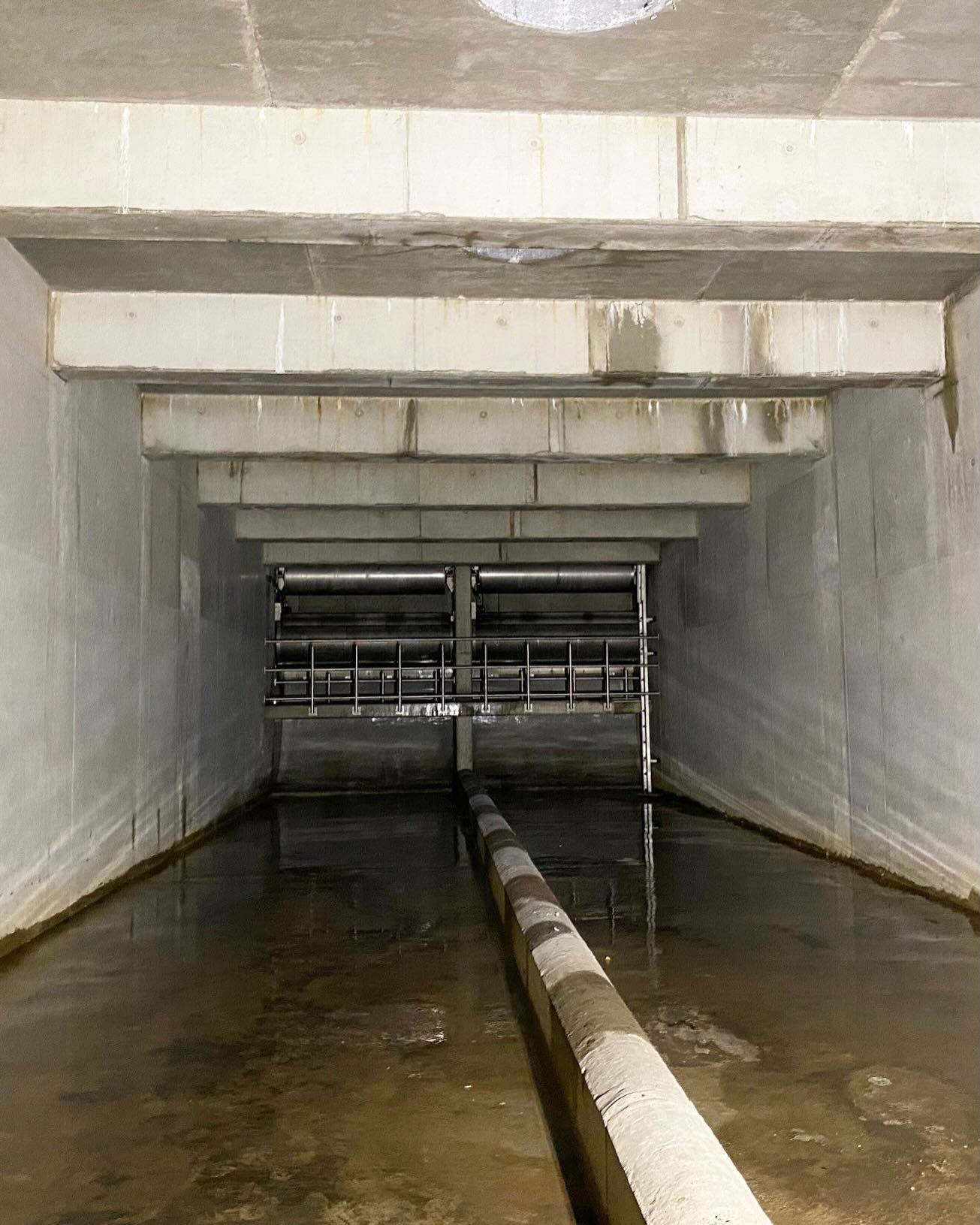 Dieser Alternativtext wurde KI-generiert: Ein rechteckiger Raum mit Betonwänden und -decke, gefüllt mit Wasser.  Ein Rohr und ein metallischer Gittermechanismus sind im Wasser sichtbar.