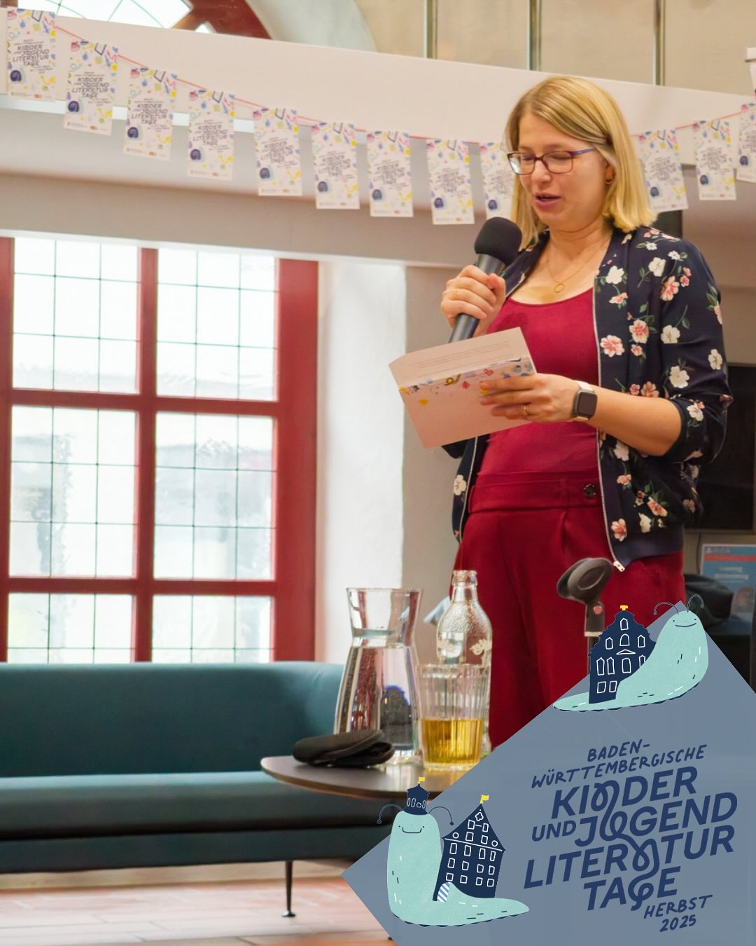 Dieser Alternativtext wurde KI-generiert: Eine Person steht vor einem Mikrofon und liest aus einem Buch vor. Im Hintergrund ist ein Fenster und eine Plakatwerbung zu sehen.