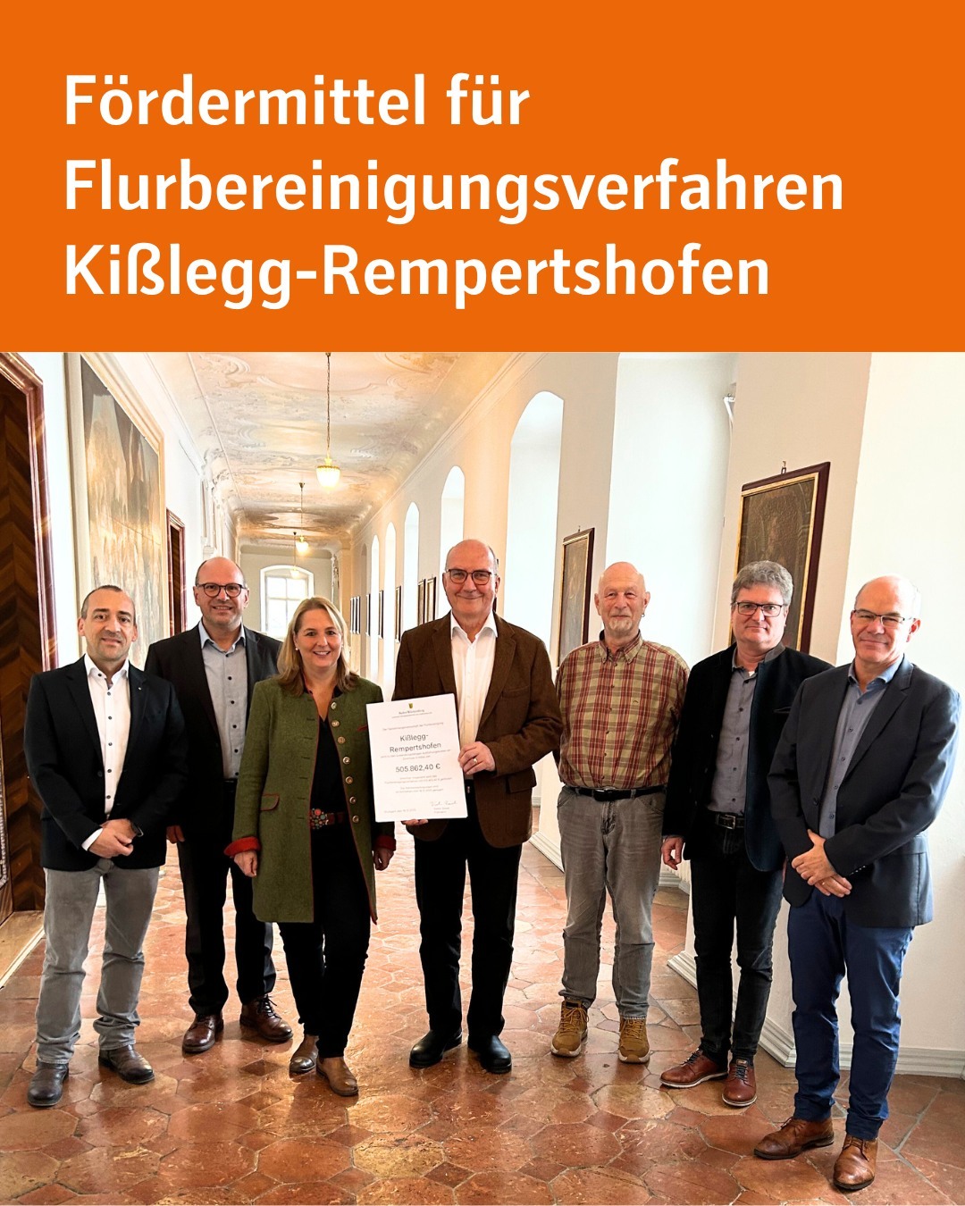 8 Personen stehen nebeneinandergereiht in einem Schlosskorridor. Eine Person hält ein Schriftstück. Text im Bild: Fördermittel für Flurbereinigungsverfahren Kißlegg-Rempertshofen