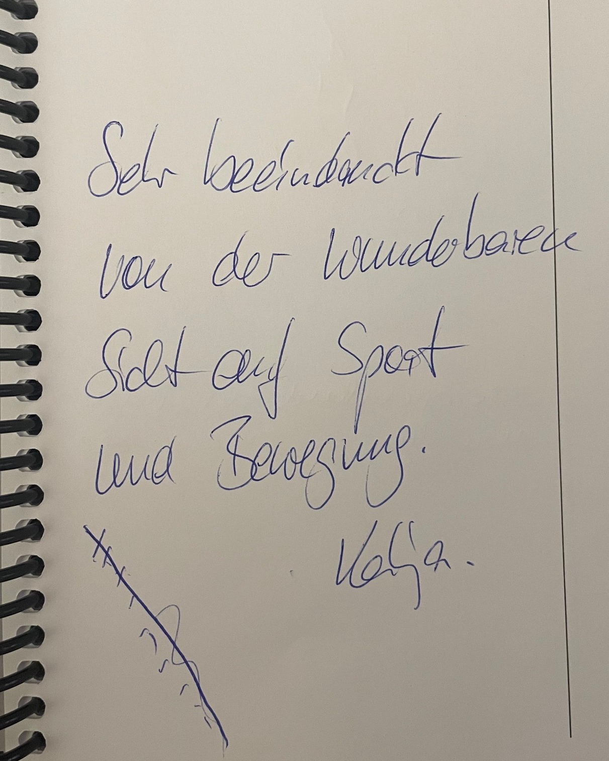 Handgeschriebene Notiz in einem Spiralblock: „Sehr beeindruckt von der Wunderbarkeit. Setzt auf Sport und Bewegung. Volker.“ Unten links ein kleines, unleserliches Strichmännchen. (KI-Alternativtext)