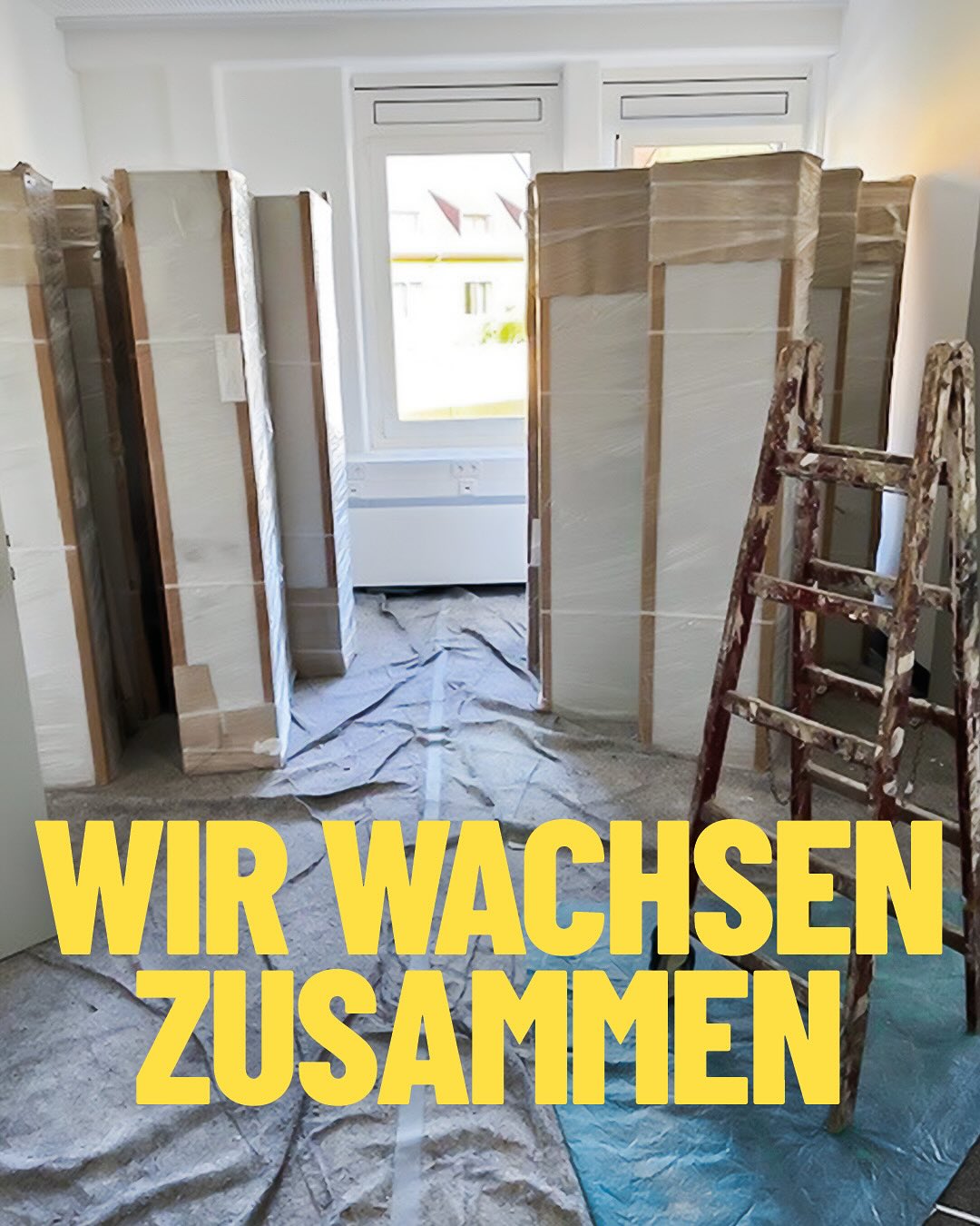 Dieser Alternativtext wurde KI-generiert: Innenraum mit mehreren Kartons und einer Leiter vor einer Tür. Im Vordergrund steht ein Text in großen gelben Buchstaben auf blauem Grund.