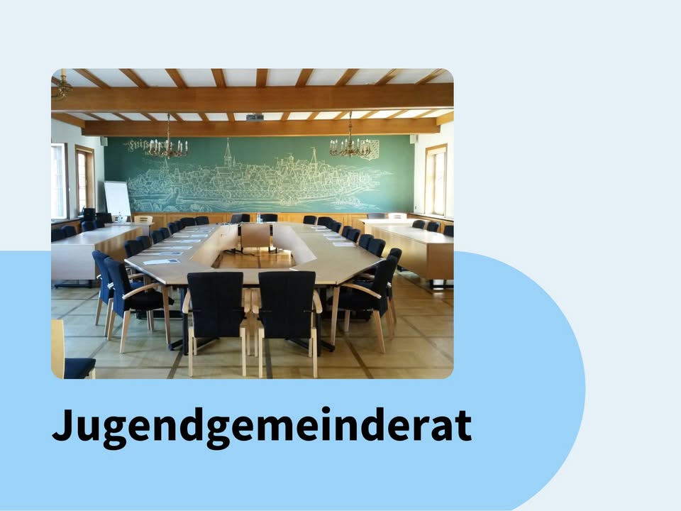 Dieser Alternativtext wurde KI-generiert: Ein heller Raum mit einem langen Konferenztisch und Stühlen. An der Wand befindet sich eine grüne Tafel mit einer Landschaftsdarstellung.