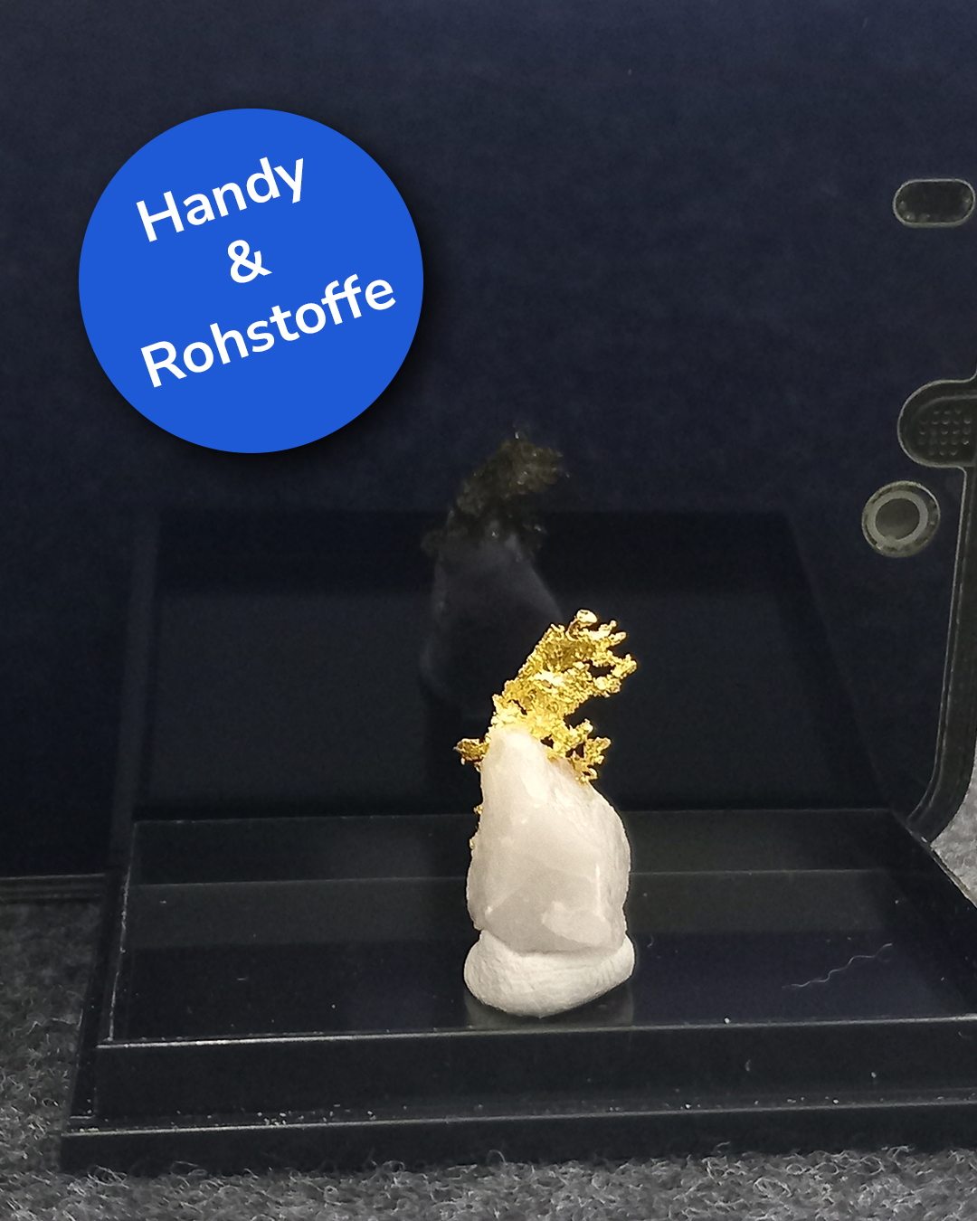 Dieser Alternativtext wurde KI-generiert: Eine Nahaufnahme zeigt ein Mineral auf einem dunklen Untergrund. Darüber befindet sich eine blaue Sprechblase mit weißer Schrift.