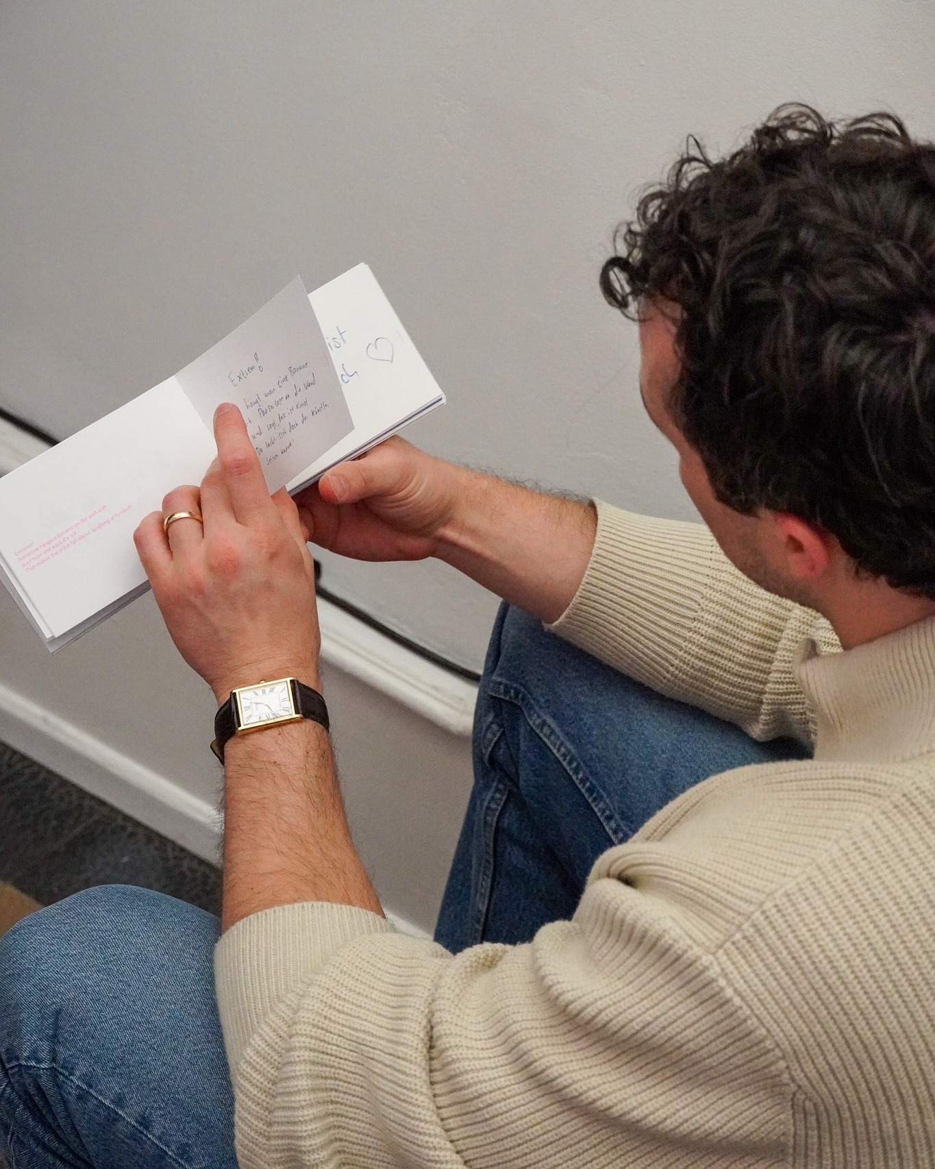 Dieser Alternativtext wurde KI-generiert: Eine Person sitzt auf einer Treppe und liest in einem offenen Buch. Auf einer Seite ist ein Herz gezeichnet.