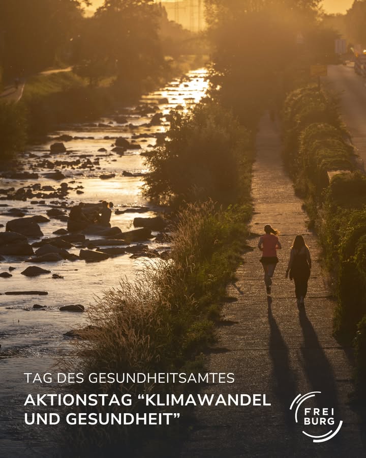 Zwei Personen spazieren bei Sonnenuntergang an einem Fluss entlang.  Im Hintergrund ist ein Radweg zu sehen.