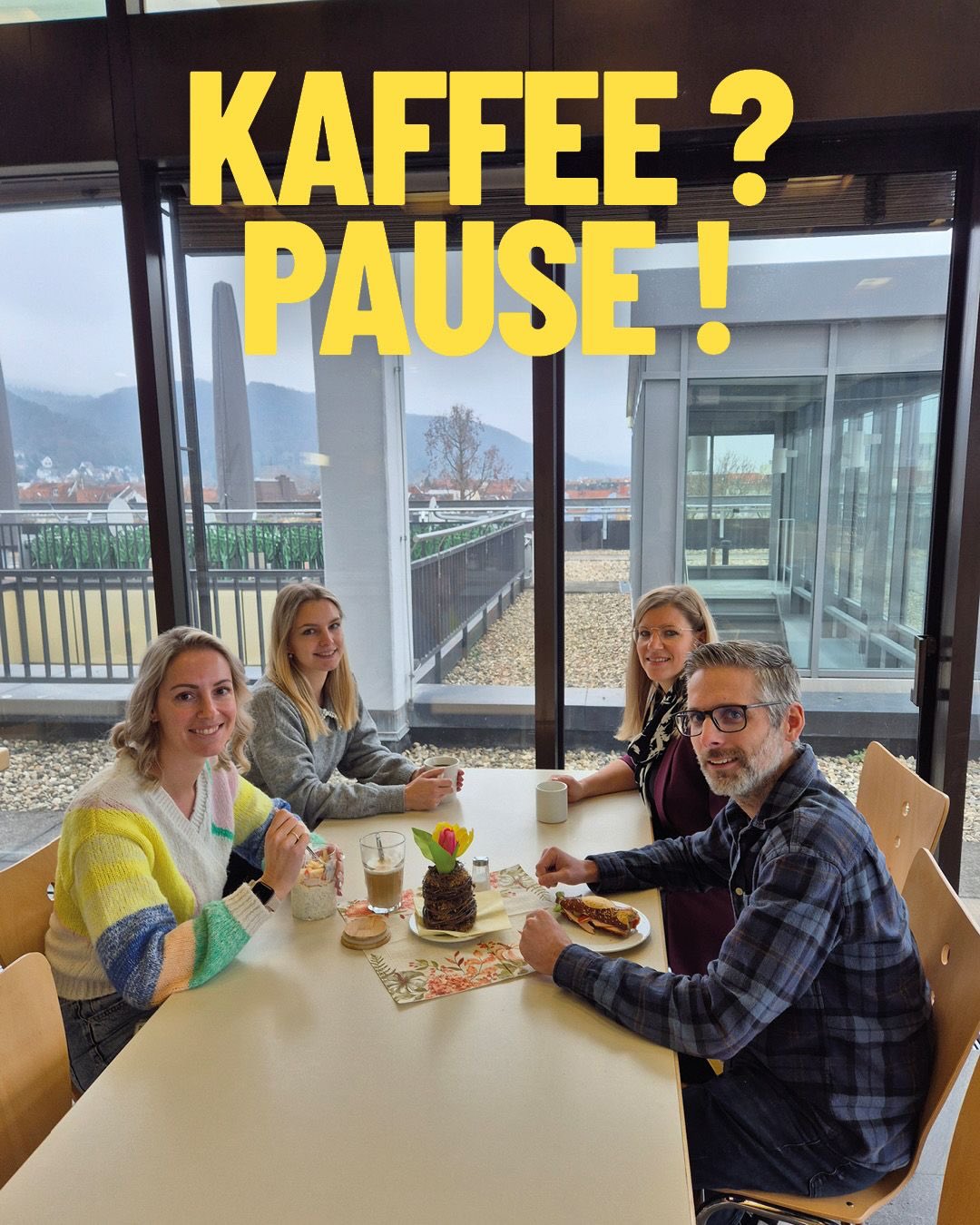 Dieser Alternativtext wurde KI-generiert: Ein Fenster zeigt eine Aussicht auf eine Stadt. Im Raum sitzen Menschen an einem Tisch mit Speisen und Getränken.