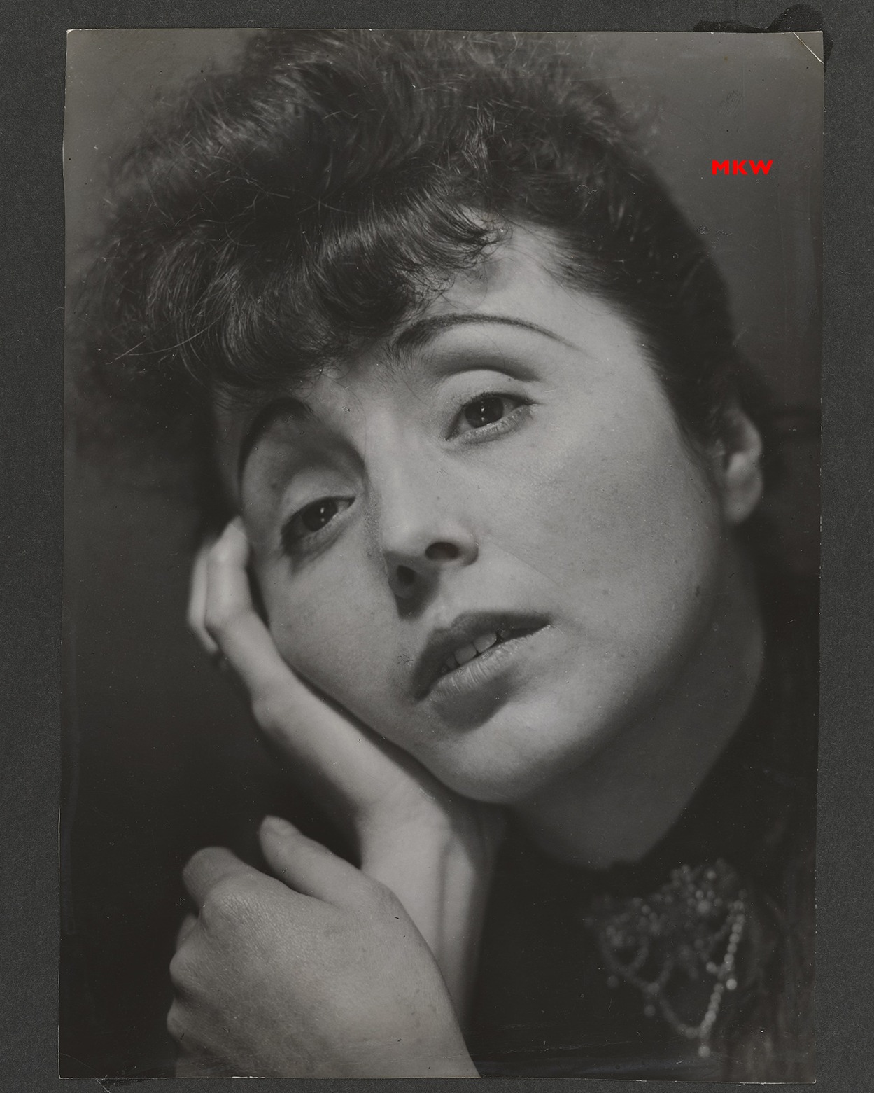 Dieser Alternativtext wurde KI-generiert: Schwarz-weißes Porträt einer Person, die mit einer Hand die Wange stützt und nachdenklich dreinblickt. Das Bild hat einen Vintage-Look und weist Gebrauchsspuren auf.