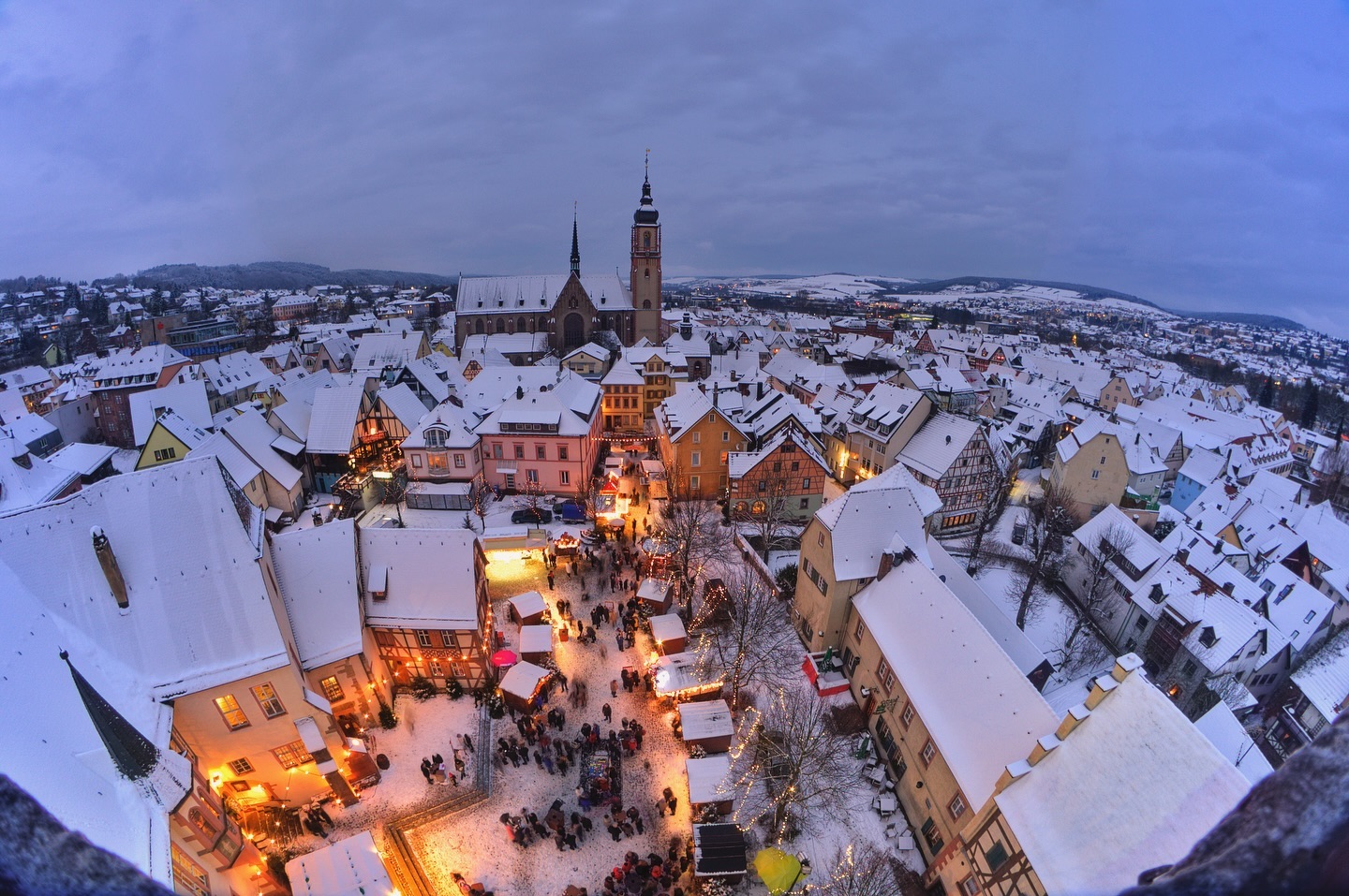 Ein verschneites Dorf bei Nacht mit Weihnachtsmarkt. Die Häuser sind mit Schnee bedeckt und beleuchtet.