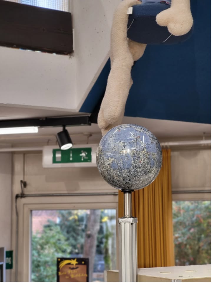 Dieser Alternativtext wurde KI-generiert: Ein dekoratives Objekt mit einer glänzenden Kugel und einem flauschigen, hellen Element darüber. Im Hintergrund sind Teile eines Raumes mit Beleuchtung und einem Fenster zu sehen.