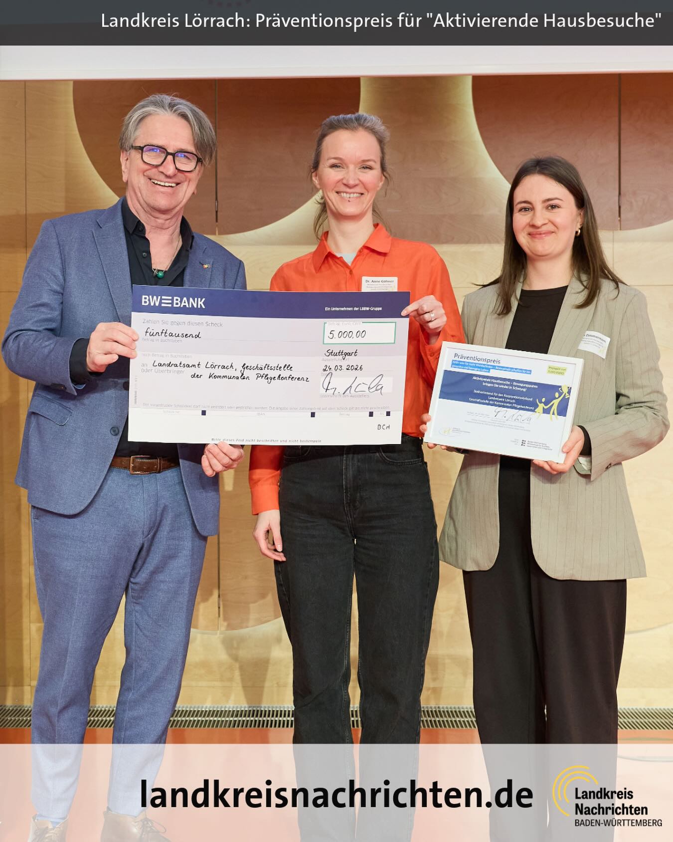 Dieser Alternativtext wurde KI-generiert: Eine farbige Aufnahme zeigt Personen, die einen übergroßen Scheck und eine Urkunde halten. Im Hintergrund ist ein Banner mit einer Aufschrift zu sehen.