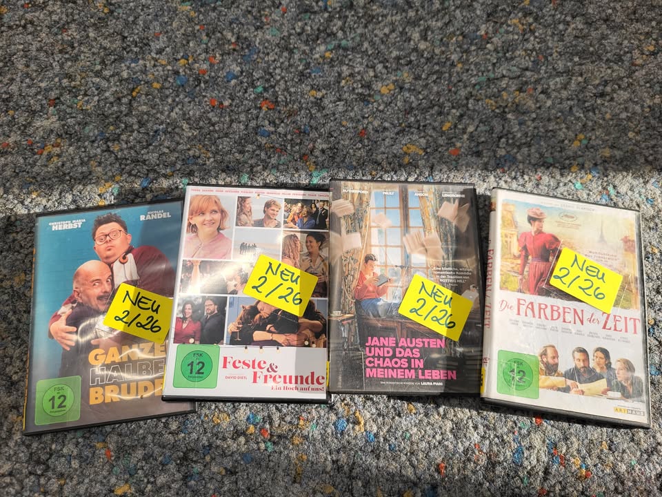 Dieser Alternativtext wurde KI-generiert: Mehrere DVD-Hüllen liegen auf einem bunten Teppich. Die Hüllen zeigen unterschiedliche Filmtitel und haben gelbe Aufkleber darauf.