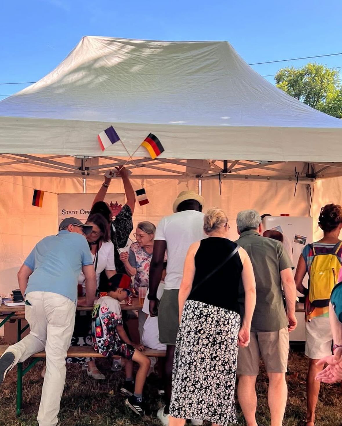 Eine Menschengruppe steht vor einem Zelt. Jemand hält kleine Flaggen von Deutschland und Frankreich hoch.