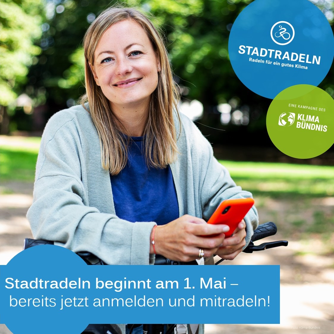 Dieser Alternativtext wurde KI-generiert: Eine Person sitzt lächelnd auf einem Fahrrad und hält ein Smartphone. Im Hintergrund befindet sich ein Logo und Text zur Förderung des Radfahrens für ein besseres Klima.