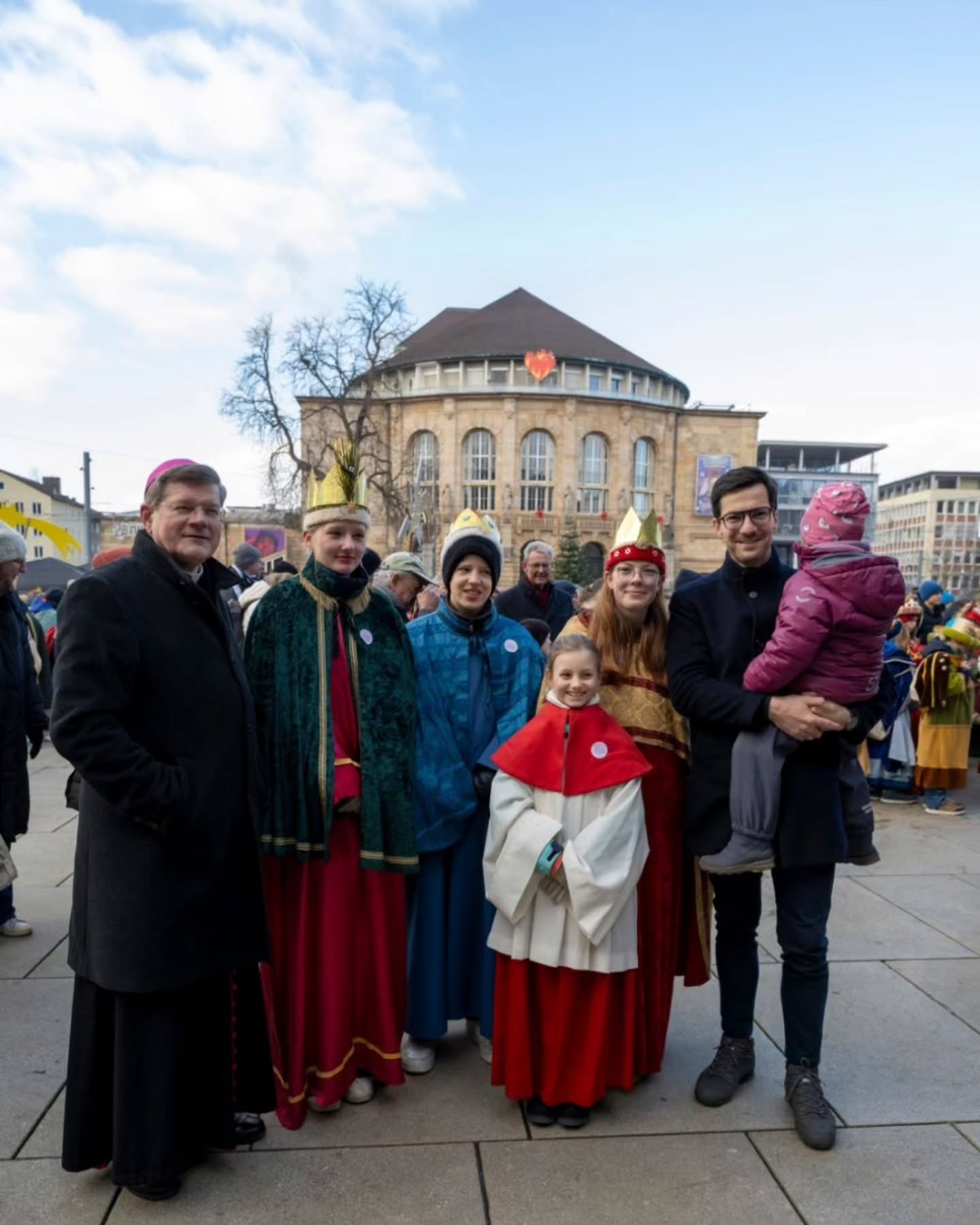 Dieser Alternativtext wurde KI-generiert: Eine Gruppe von Personen steht vor einem Gebäude mit einer Kuppel. Einige tragen festliche Kostüme oder Hüte.