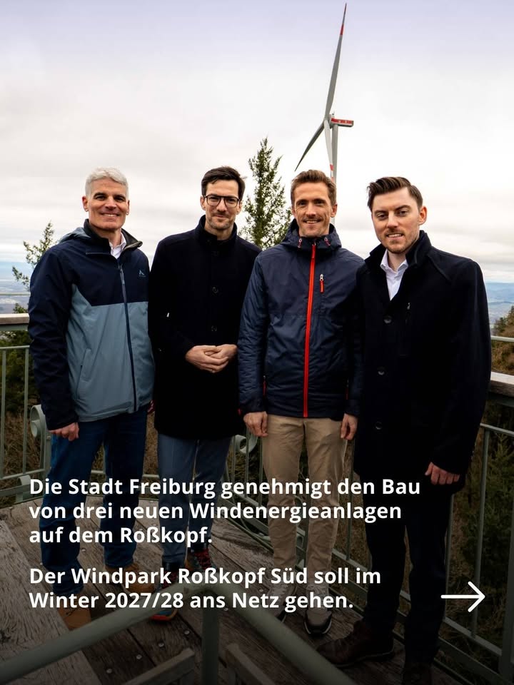 Dieser Alternativtext wurde KI-generiert: Farbfoto zeigt mehrere Personen, die im Freien vor einem Hintergrund aus Bäumen und Windkraftanlagen posieren. Im Vordergrund befindet sich Text, der Informationen zu einem Windparkprojekt enthält.