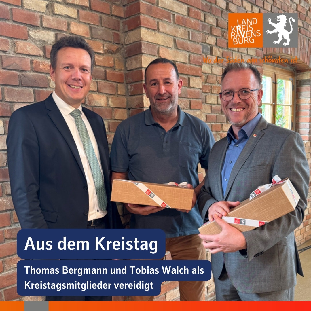 Drei lächelnde Personen stehen vor einer Backsteinwand und halten Geschenke. Oben rechts befindet sich ein Logo.