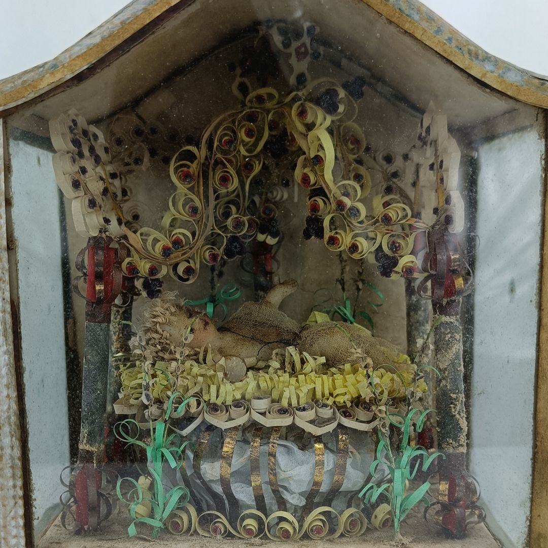 Dieser Alternativtext wurde KI-generiert: Eine Nahaufnahme eines alten, verzierten Schaukastens mit einer kunstvollen Papiercollage im Inneren. Die Collage zeigt verschlungene Ornamente und eine detaillierte Szene.