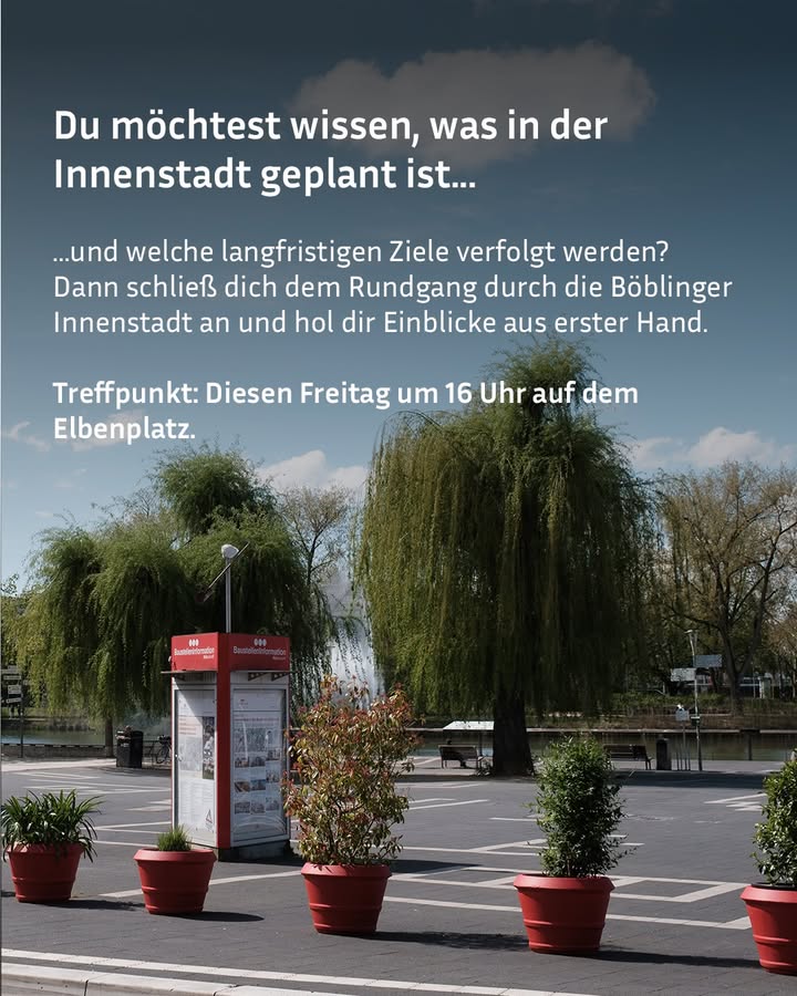 Dieser Alternativtext wurde KI-generiert: Ein belebter Platz mit Bäumen, Bänken und einer Informationstafel. Im Hintergrund sind Gebäude und ein grauer Himmel zu sehen.
