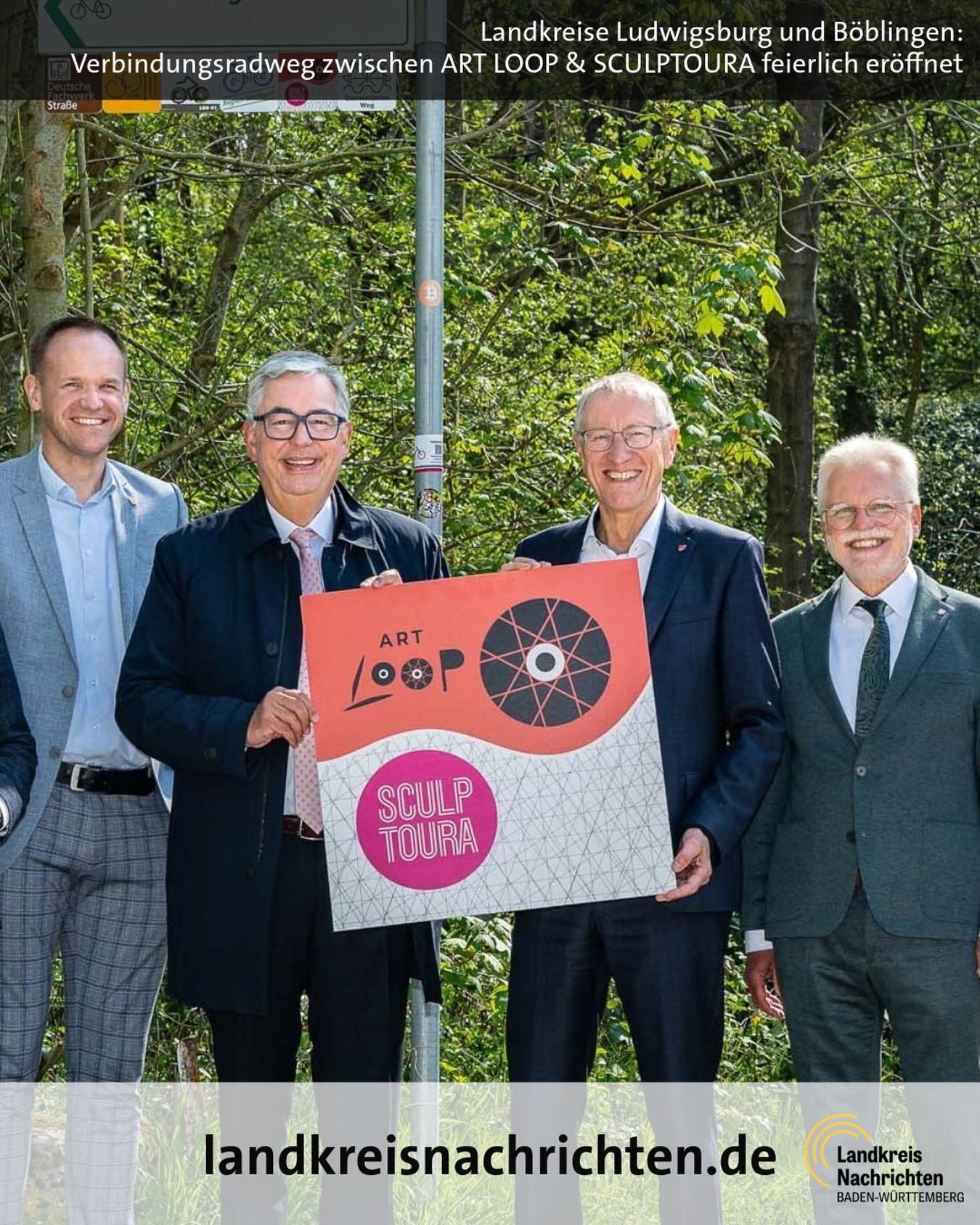 Dieser Alternativtext wurde KI-generiert: Eine farbige Aufnahme zeigt Menschen, die mit einem Kunstwerk posieren. Im Hintergrund ist eine Straße mit Bäumen und ein Zeichen zu sehen.