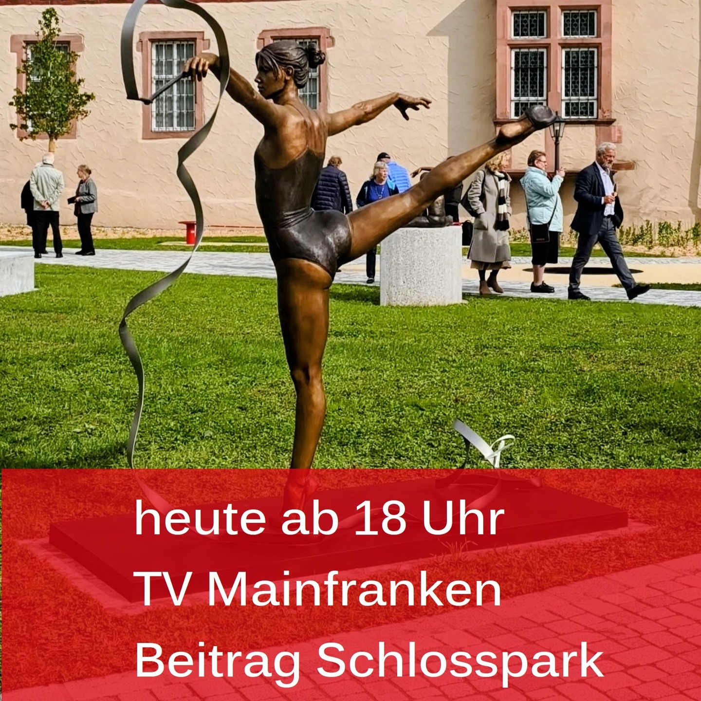 Dieser Alternativtext wurde KI-generiert: Eine bronzefarbene Skulptur einer tanzenden Figur steht im Vordergrund. Im Hintergrund sind Gebäude und Personen zu sehen, sowie ein roter Banner mit Text.