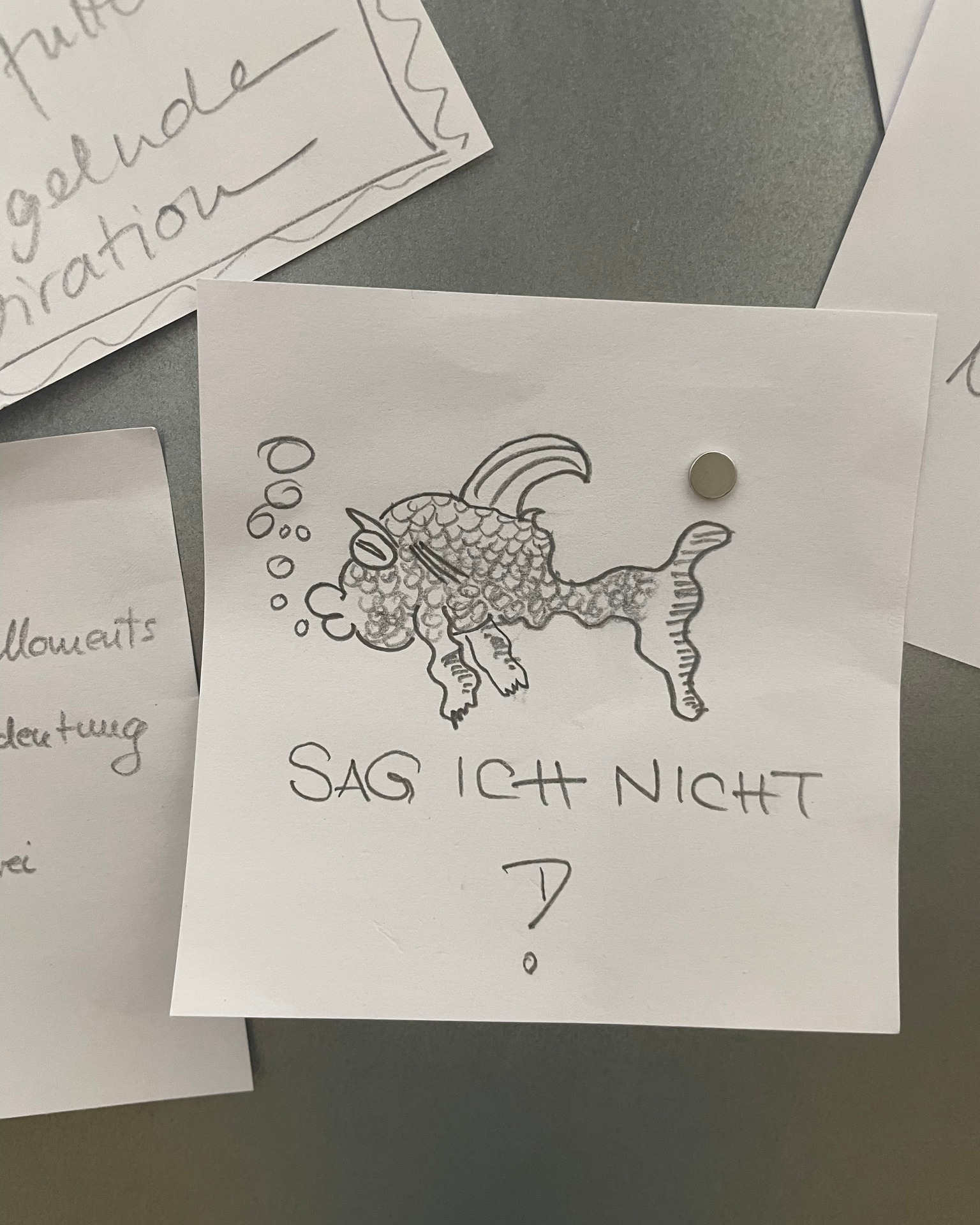 Dieser Alternativtext wurde KI-generiert: Ein handgezeichnetes Bild eines Wesens mit Hörnern und Flügeln ist an eine Pinnwand geheftet. Unterhalb der Zeichnung befindet sich ein Text.