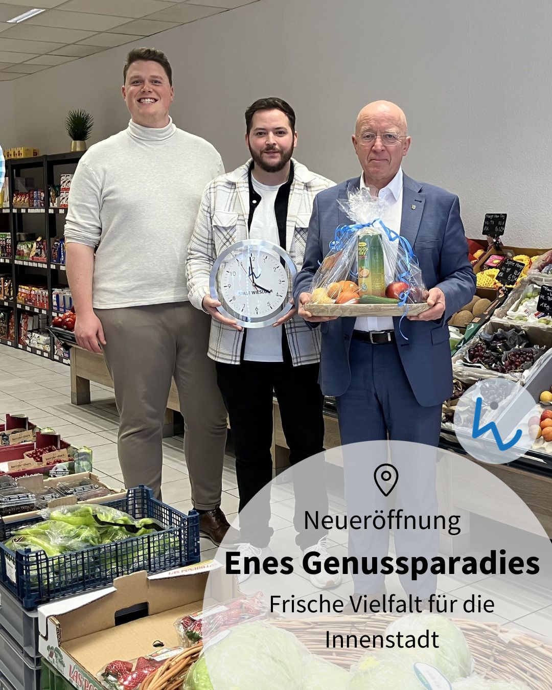 Dieser Alternativtext wurde KI-generiert: Mehrere Personen stehen in einem Lebensmittelgeschäft vor einem Regal mit Obst und Gemüse sowie einer großen Uhr. Im Vordergrund befindet sich ein Werbeaufsteller für eine Neueröffnung.