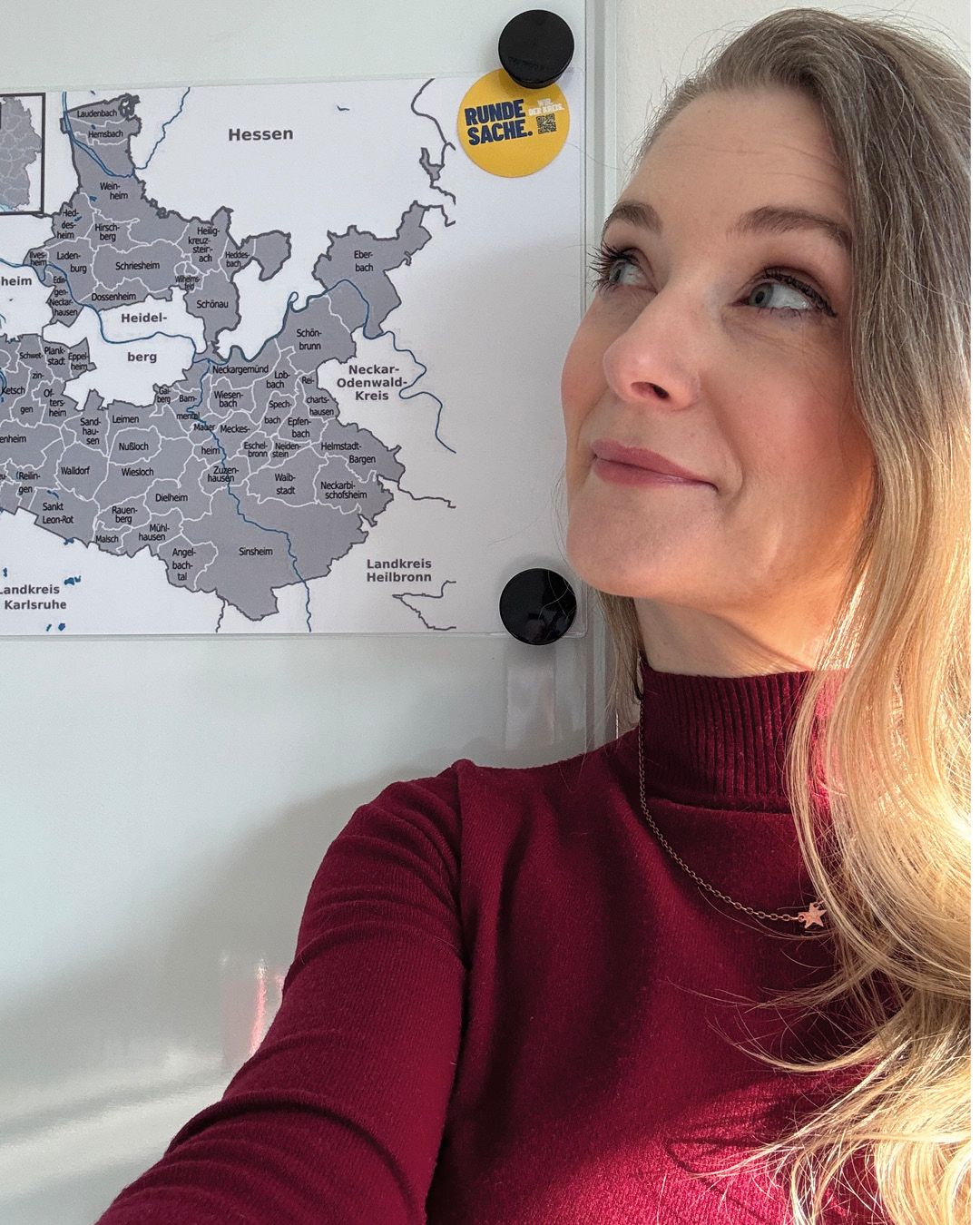 Dieser Alternativtext wurde KI-generiert: Eine Person mit langen Haaren betrachtet eine Karte von Deutschland, die an der Wand hängt. Im Bild ist außerdem ein runder Aufkleber zu sehen.