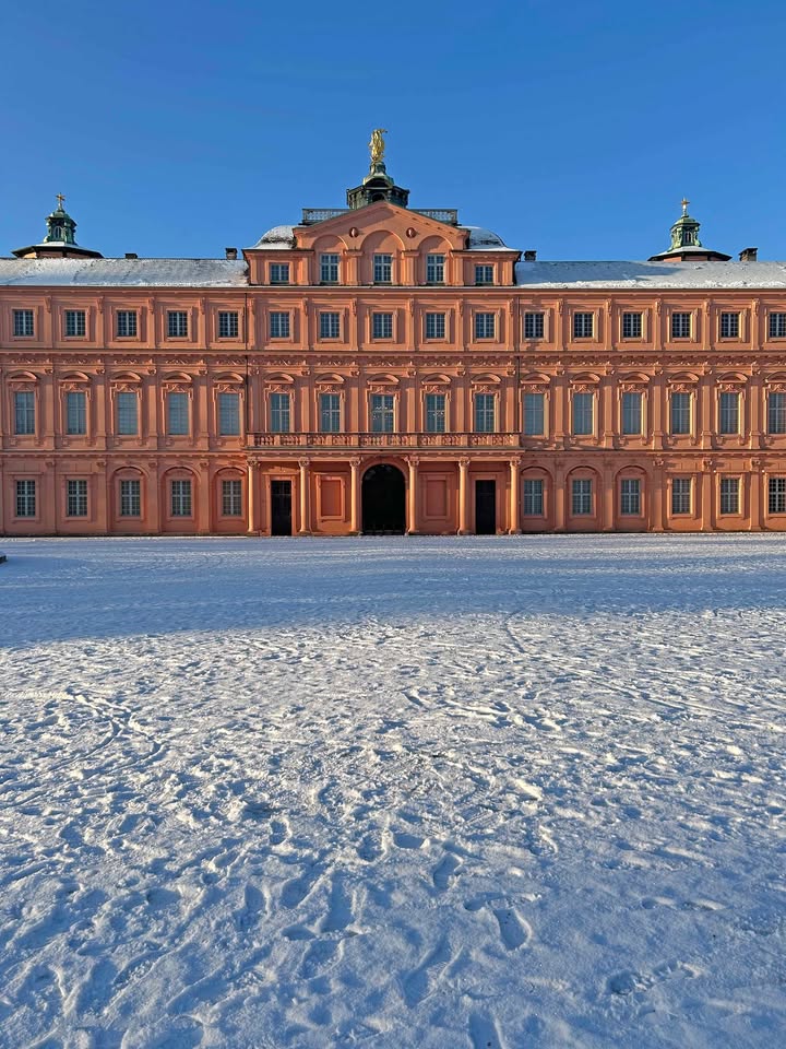Dieser Alternativtext wurde KI-generiert: Ein großes Gebäude mit architektonischen Details steht vor einem mit Schnee bedeckten Platz. Das Bild ist bei hellem Tageslicht aufgenommen.