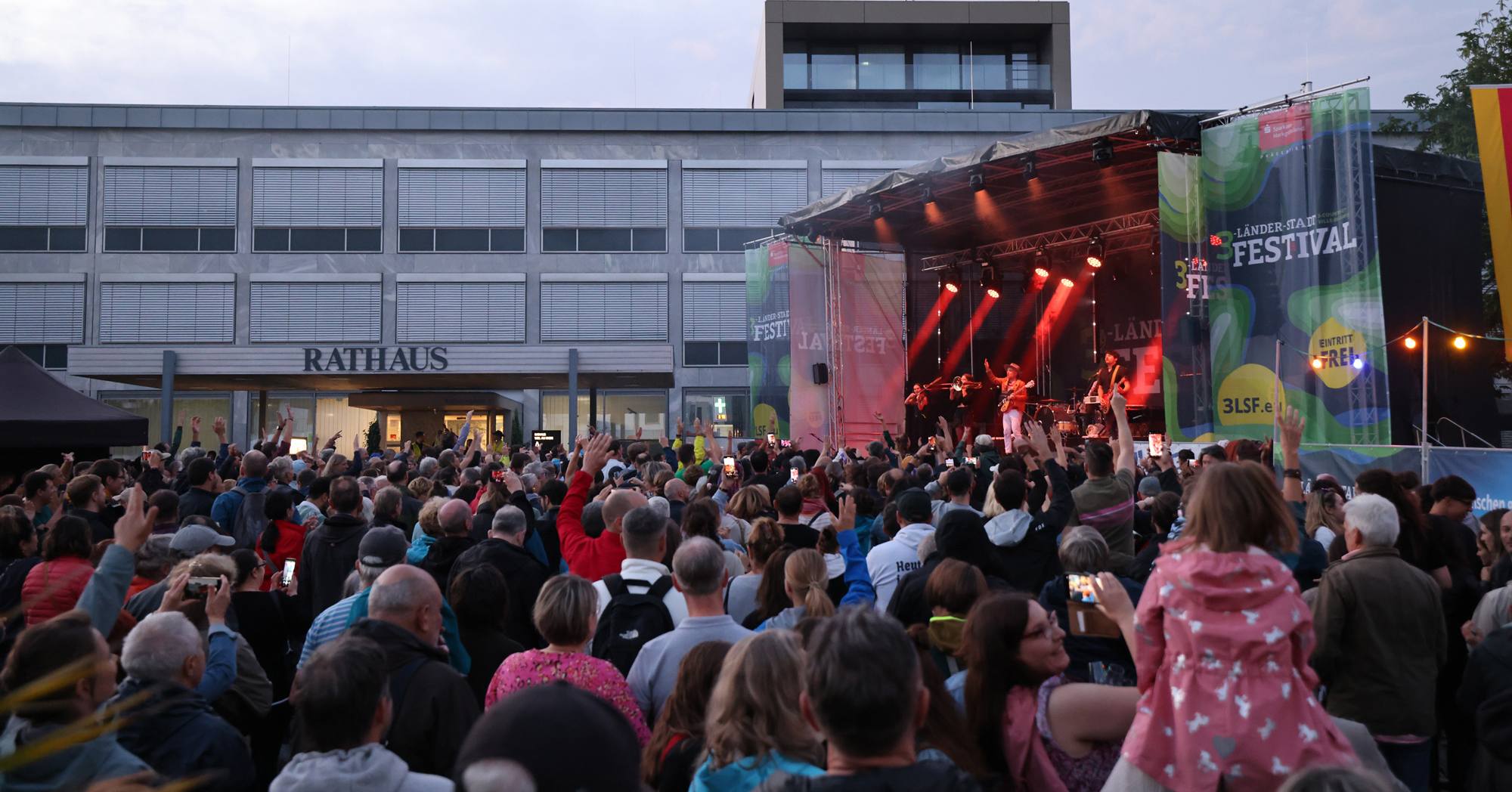 Auf einer grossen Bühne spielt eine Band. Vor der Bühne tanzen viele Menschen vor Freude.