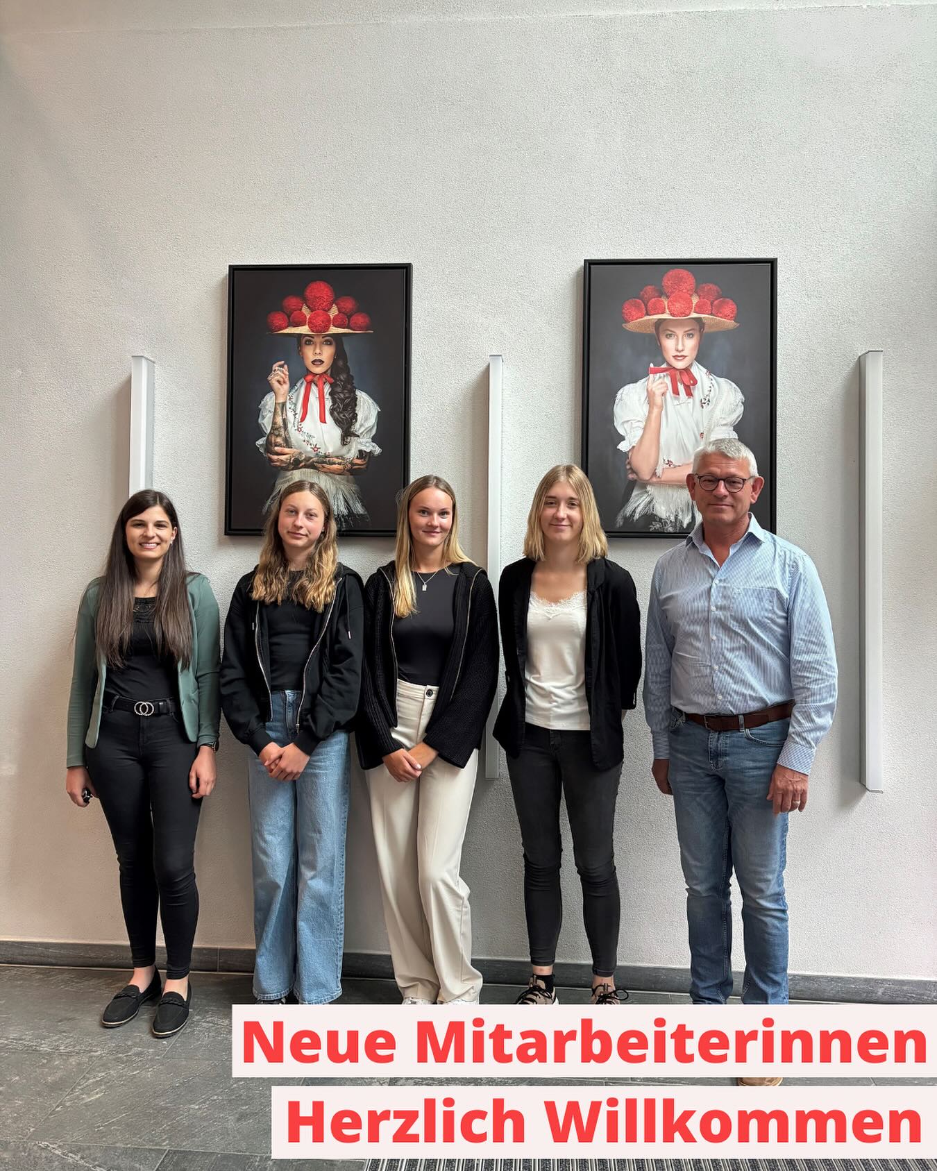 Eine Gruppe von Personen steht vor einer hellen Wand mit zwei Porträtbildern. Ein Schild unter der Gruppe trägt eine Begrüßungsbotschaft.