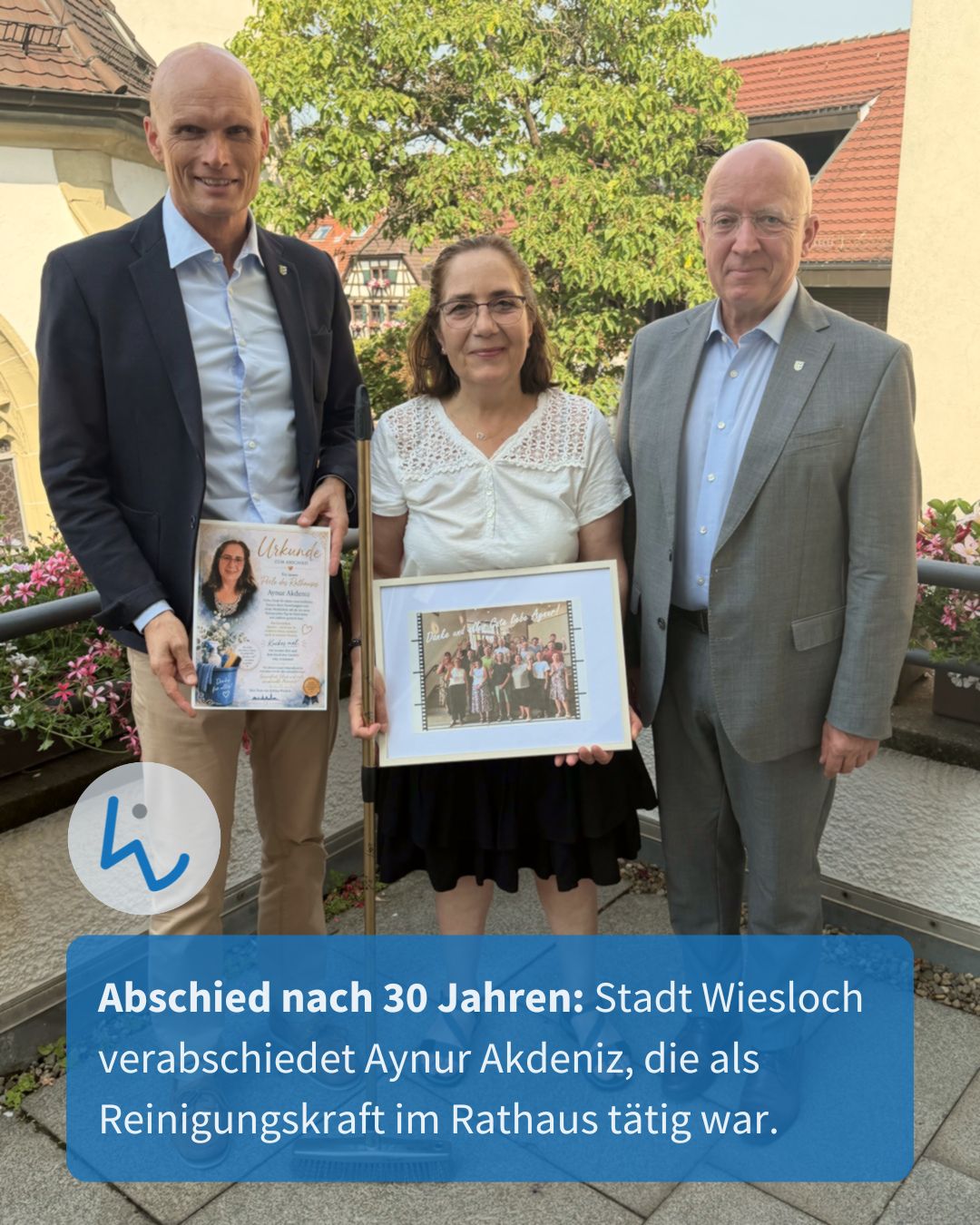 Drei Personen stehen im Freien. Die Person in der Mitte hält ein gerahmtes Gruppenfoto und einen weißen Blindenstock, während die Person links eine Urkunde hält. Ein Textfeld unten lautet: "Abschied nach 30 Jahren: Stadt Wiesloch verabschiedet Aynur Akdeniz, die als Reinigungskraft im Rathaus tätig war." (KI-Alternativtext)