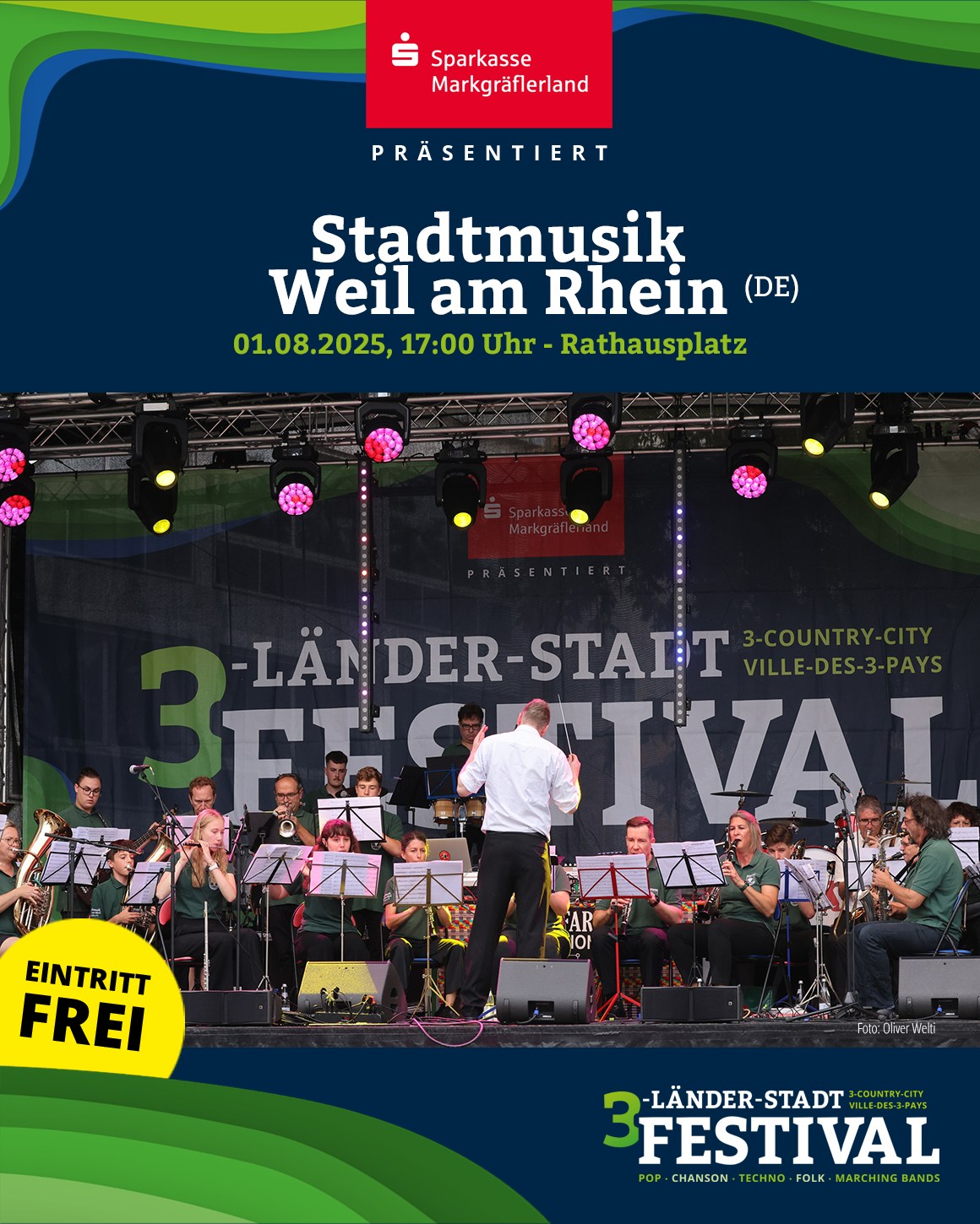 Eine Musikgruppe spielt auf einer Bühne vor einer großen Werbefläche. Im Vordergrund steht der Dirigent.