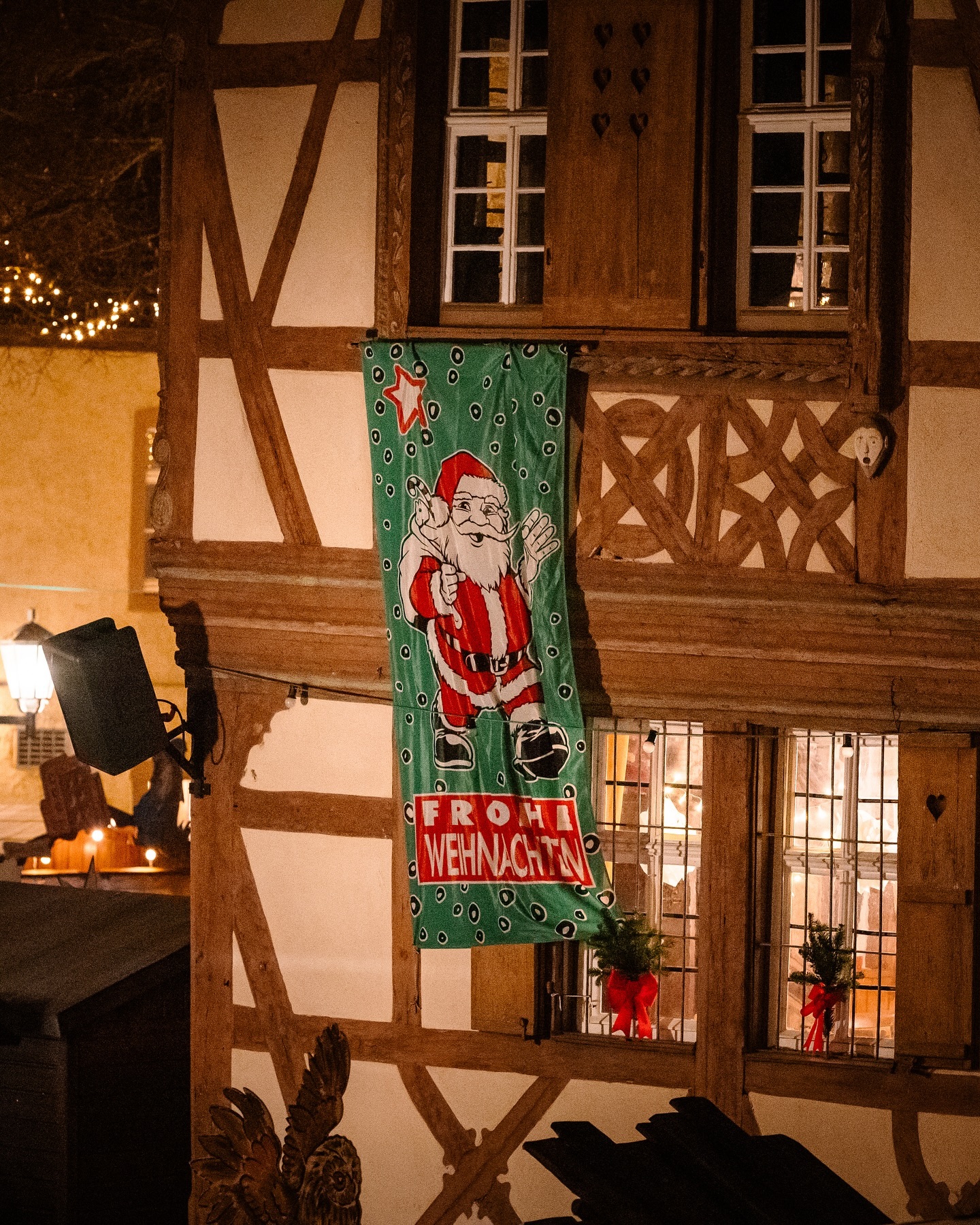 Ein grünes Banner mit weihnachtlichem Motiv schmückt ein Fachwerkhaus. Im Fenster sind weihnachtliche Dekorationen zu sehen.