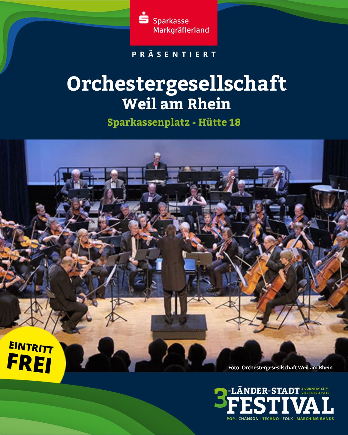 Das Foto zeigt ein Orchester, das auf einer Bühne spielt. Davor befinden sich Personen, die dem Auftritt zusehen.