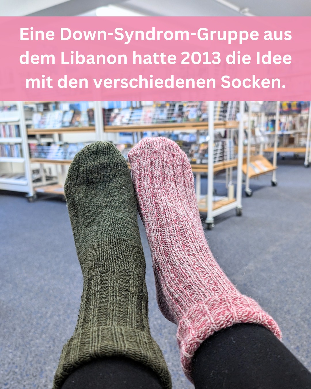 Zwei verschiedenfarbige Socken liegen übereinander. Im Hintergrund sieht man Bücherregale.