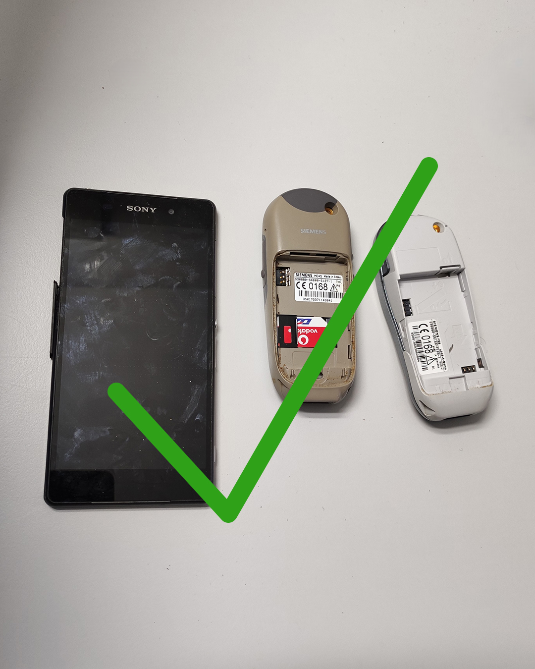 Dieser Alternativtext wurde KI-generiert: Zwei alte Mobiltelefone und eine Speicherkarte liegen nebeneinander auf einer hellen Oberfläche. Ein grünes Häkchen und ein Kreuz überlagern das Bild.