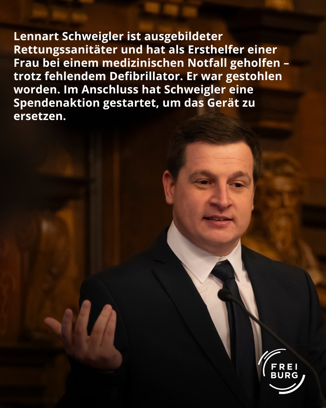 Dieser Alternativtext wurde KI-generiert: Schwarz-weißes Porträt einer Person mit dunklem Haar in einem dunklen Anzug. Ein Logo ist im unteren rechten Bereich des Bildes zu sehen.