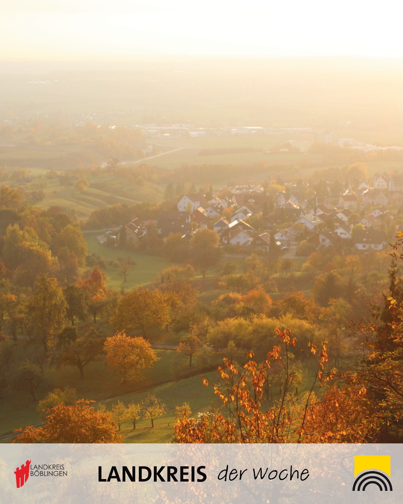 Dieser Alternativtext wurde KI-generiert: Ein hügeliges Land mit herbstlichen Bäumen und Häusern. Die Aufnahme ist in warmen, goldenen Farbtönen gehalten.