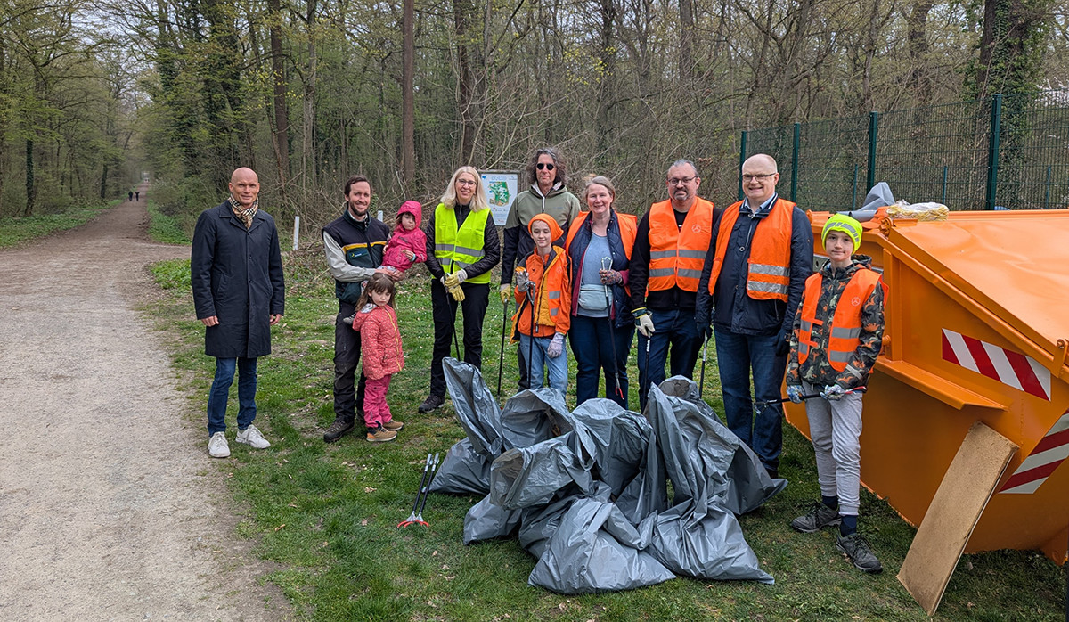 Dieser Alternativtext wurde KI-generiert: Eine Gruppe von Menschen steht auf einem Weg in einer Parklandschaft. Sie tragen Westen und halten Müllsäcke, möglicherweise bei einer Reinigungsaktion.