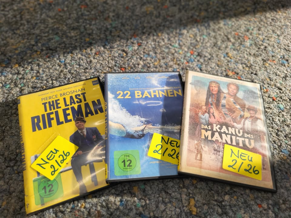 Dieser Alternativtext wurde KI-generiert: Drei DVD-Hüllen liegen nebeneinander auf einem farbenfrohen Teppich. Die Hüllen zeigen verschiedene Filmtitel und Altersfreigaben.