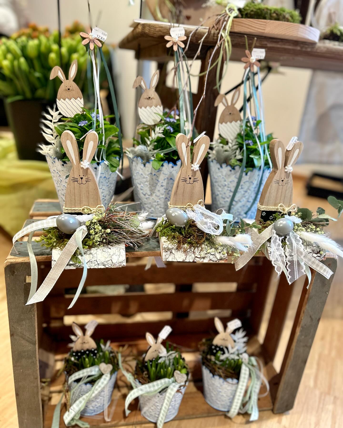 Dekorative Objekte mit Hasenmotiven und Pflanzen sind auf einem Holzkasten arrangiert. Es handelt sich um saisonale Dekorationen.