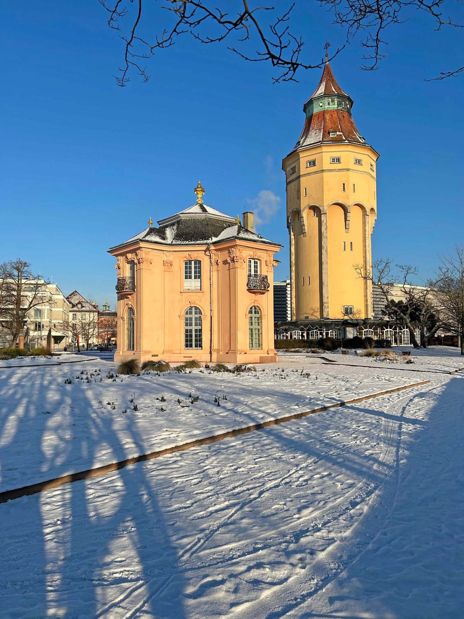 Dieser Alternativtext wurde KI-generiert: Ein Gebäude mit mehreren Stockwerken und einer Kuppel steht vor blauem Himmel. Schnee bedeckt den Boden und wirft lange Schatten.