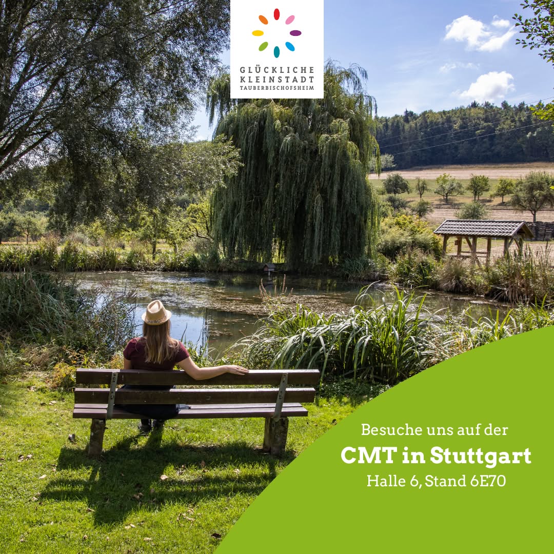 Dieser Alternativtext wurde KI-generiert: Farbfoto einer Person, die auf einer Bank an einem Teich sitzt. Im Hintergrund ist eine Wiese und Bäume zu sehen.