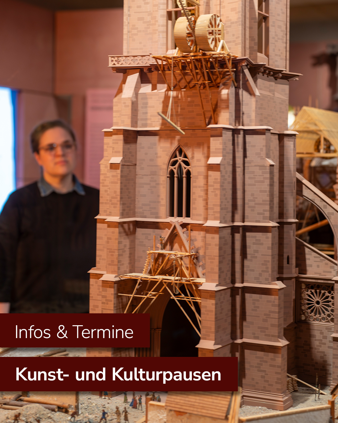 Dieser Alternativtext wurde KI-generiert: Ein detailliertes Modell einer gotischen Kathedrale steht im Fokus, während im Hintergrund eine Person zu sehen ist. Das Foto wurde in einem Museum oder Ausstellungsraum aufgenommen.