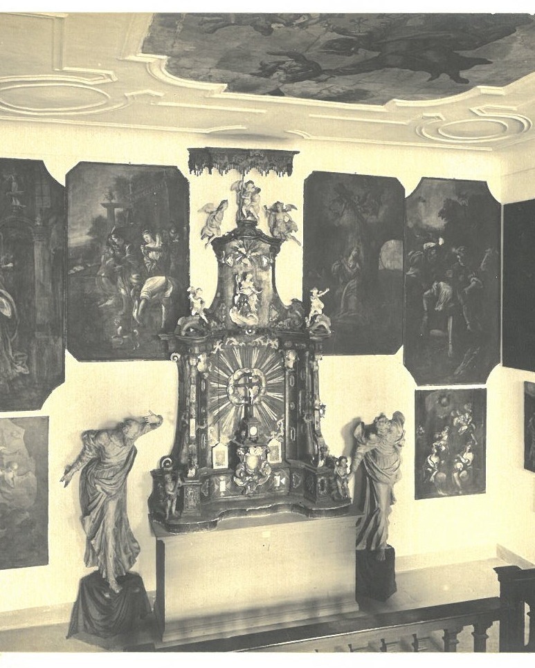 Dieser Alternativtext wurde KI-generiert: Schwarz-weißes Bild einer Innenansicht mit religiösen Kunstwerken an den Wänden. Ein Altar steht im Zentrum des Raumes, umgeben von Gemälden und Skulpturen.