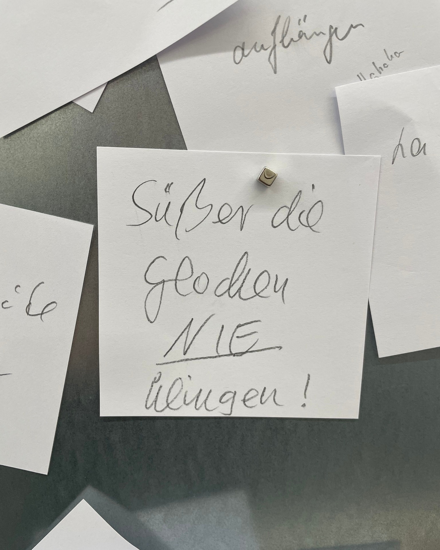 Dieser Alternativtext wurde KI-generiert: Mehrere handbeschriebene Zettel liegen auf einer grauen Oberfläche. Der Text ist in Schreibschrift auf den Zetteln zu sehen.